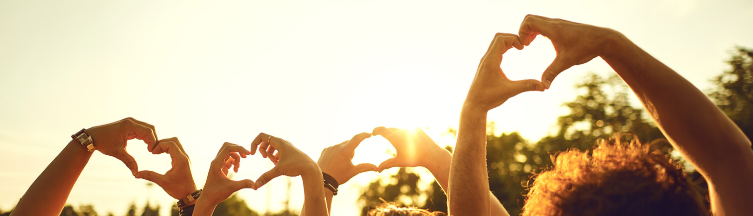 Hands of group friends in the shape of a heart against the sunset.
